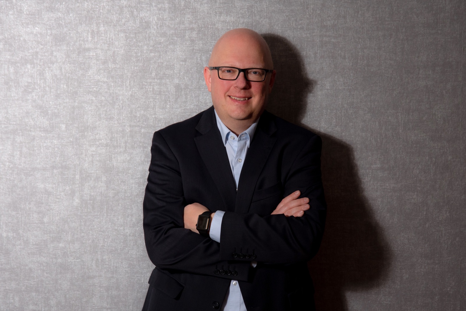 Thorsten Jungmann, ein Mann mit kurzen, hellen Haaren, dunkler Brille, hellblauem Hemd und dunkelblauem Sakko, vor einem grauen Fotohintergrund